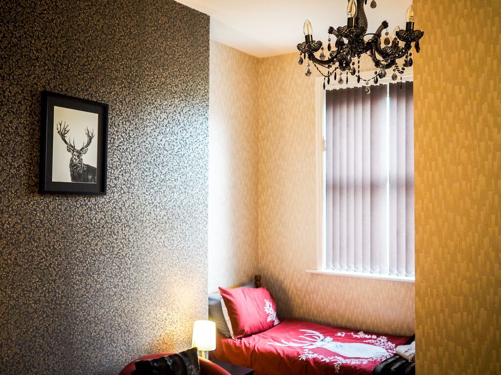 A bedroom with a bed, a chandelier, a window with curtains, and a framed picture on the wall.