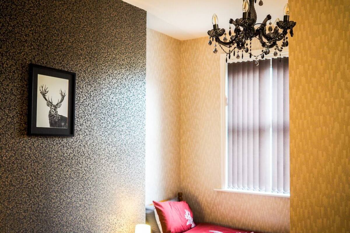 A bedroom with a bed, a chandelier, a window with curtains, and a framed picture on the wall.
