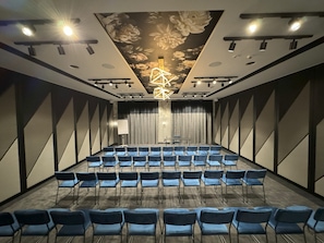 A conference room with rows of chairs, a stage, a floral ceiling design, and a modern light fixture. - Hotel Moderno (Poznan)