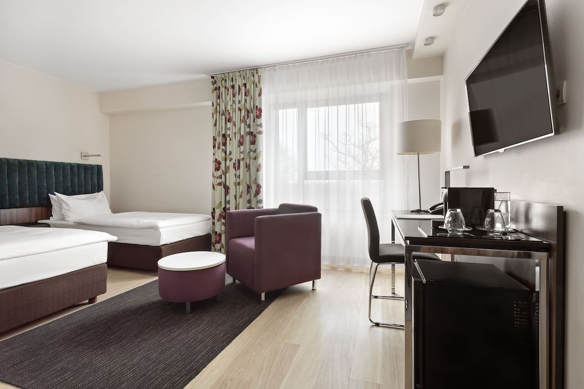 A hotel room with a bed, a desk with a computer, a chair, and a television.