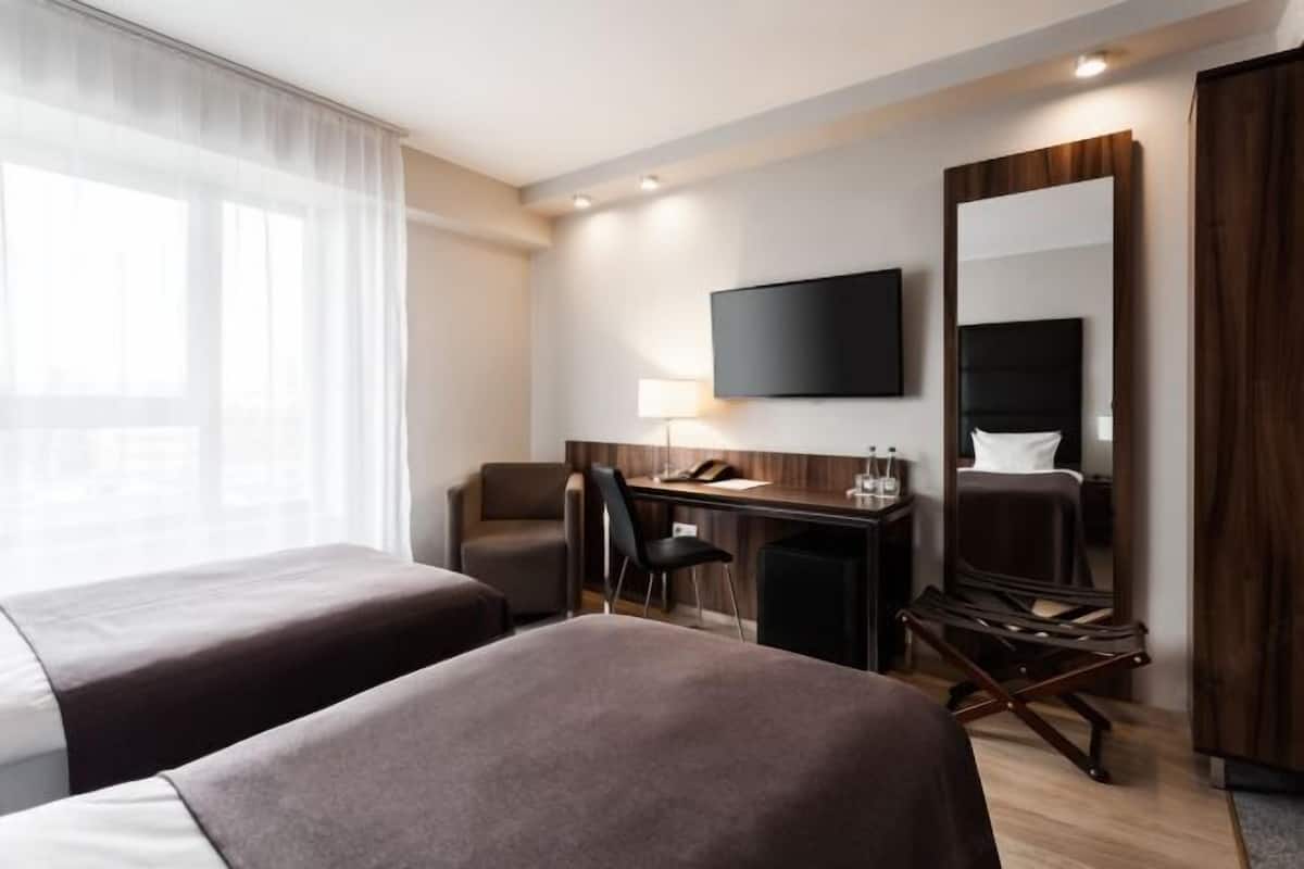 A hotel room with two beds, a desk, a chair, a TV, and a mirror.