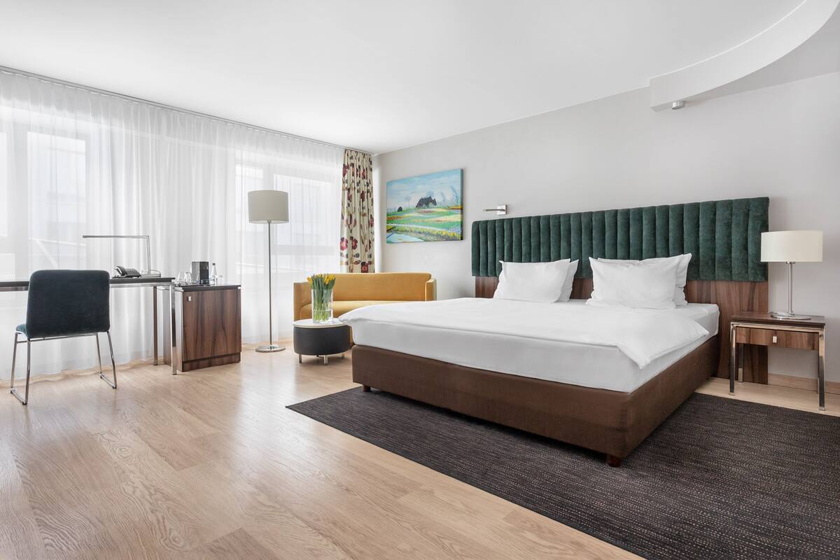 Una moderna camera d'albergo con un letto grande, una scrivania, una sedia, una lampada e un quadro appeso al muro.