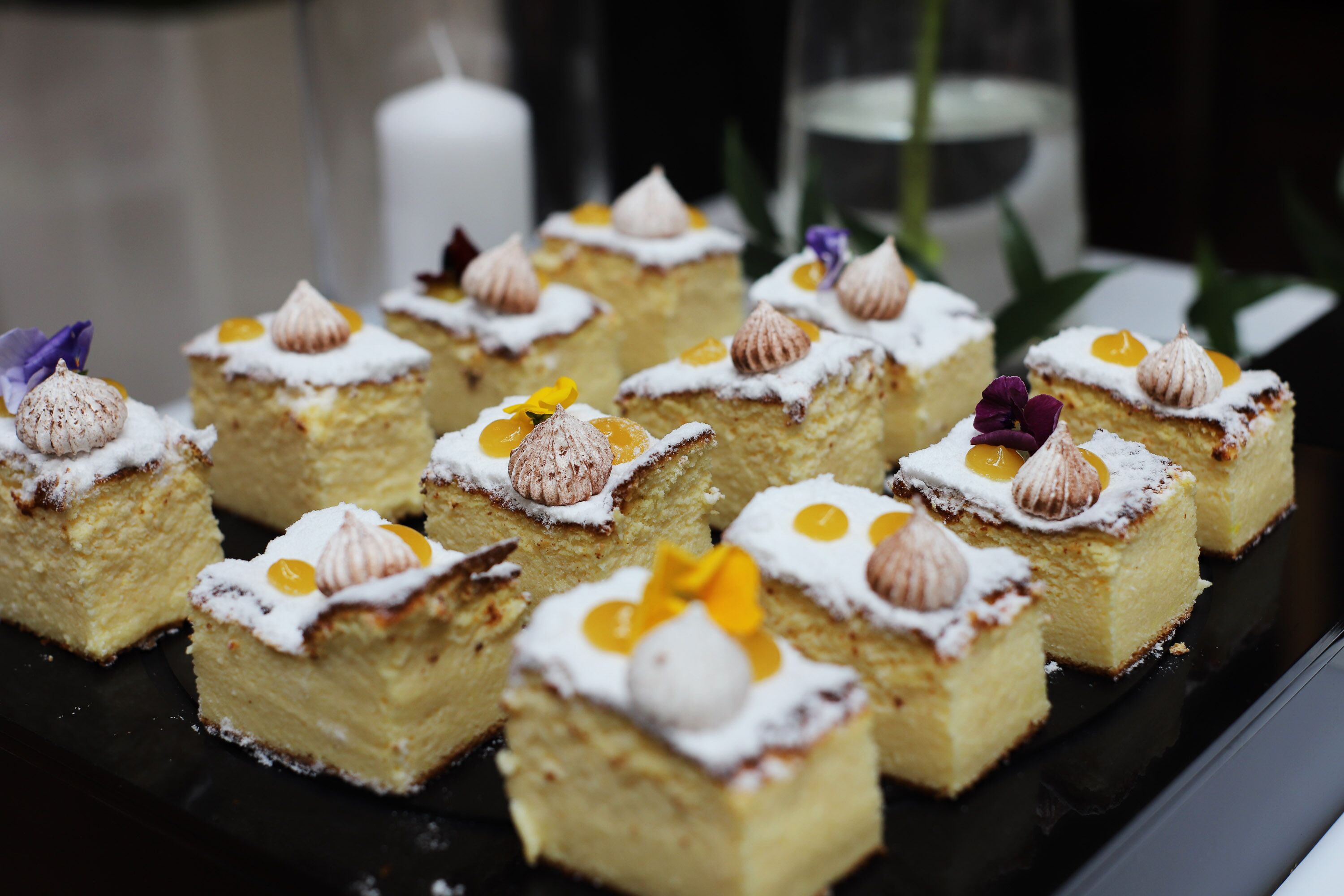 A tray of square desserts with white frosting and decorative toppings.