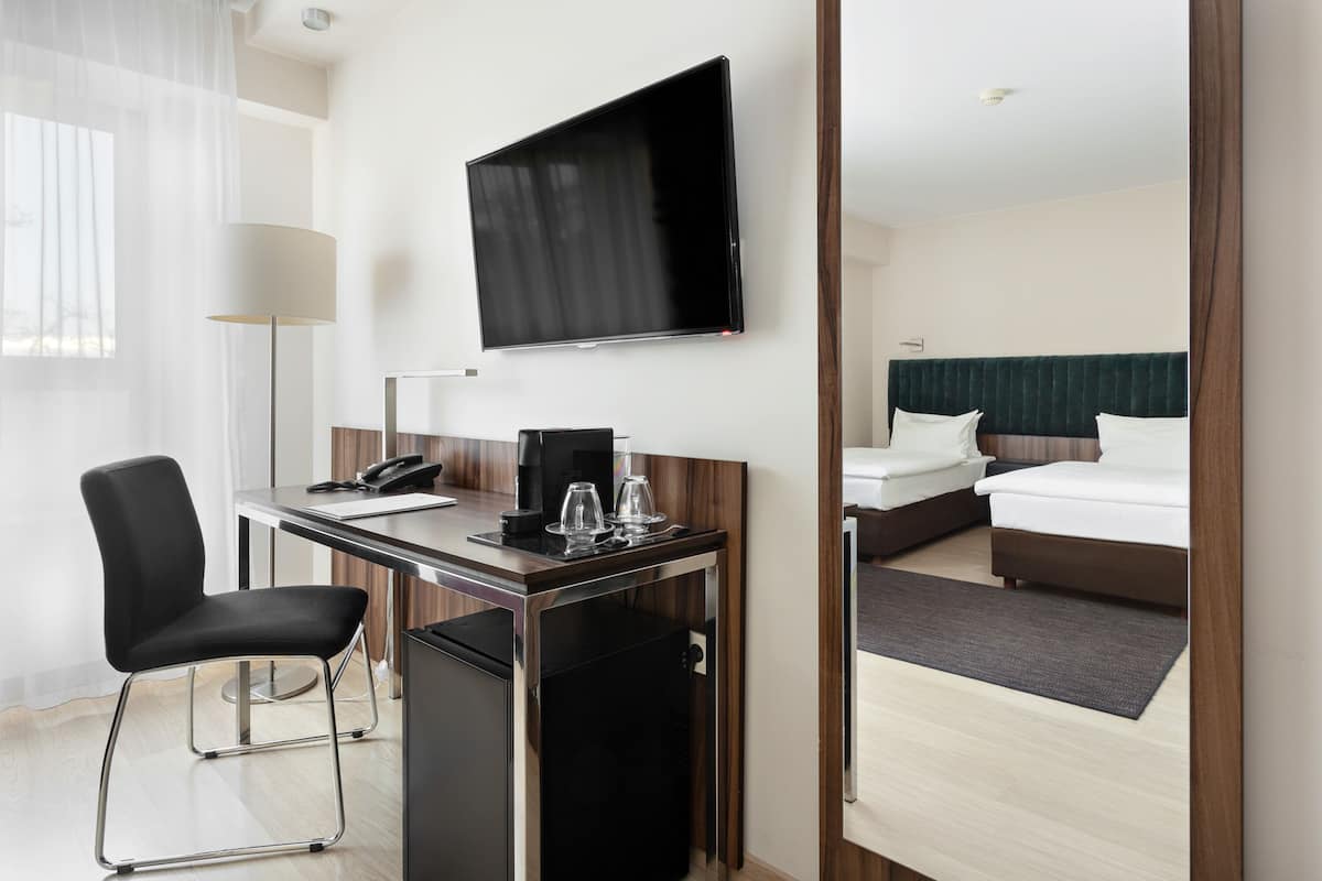 A hotel room with a desk, chair, television, bed, and a small refrigerator.