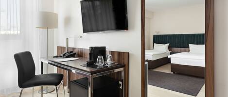 A hotel room with a desk, chair, television, bed, and a small refrigerator.