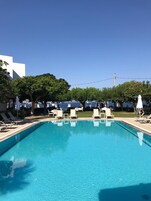 Una piscina al aire libre, sombrillas, sillones reclinables de piscina