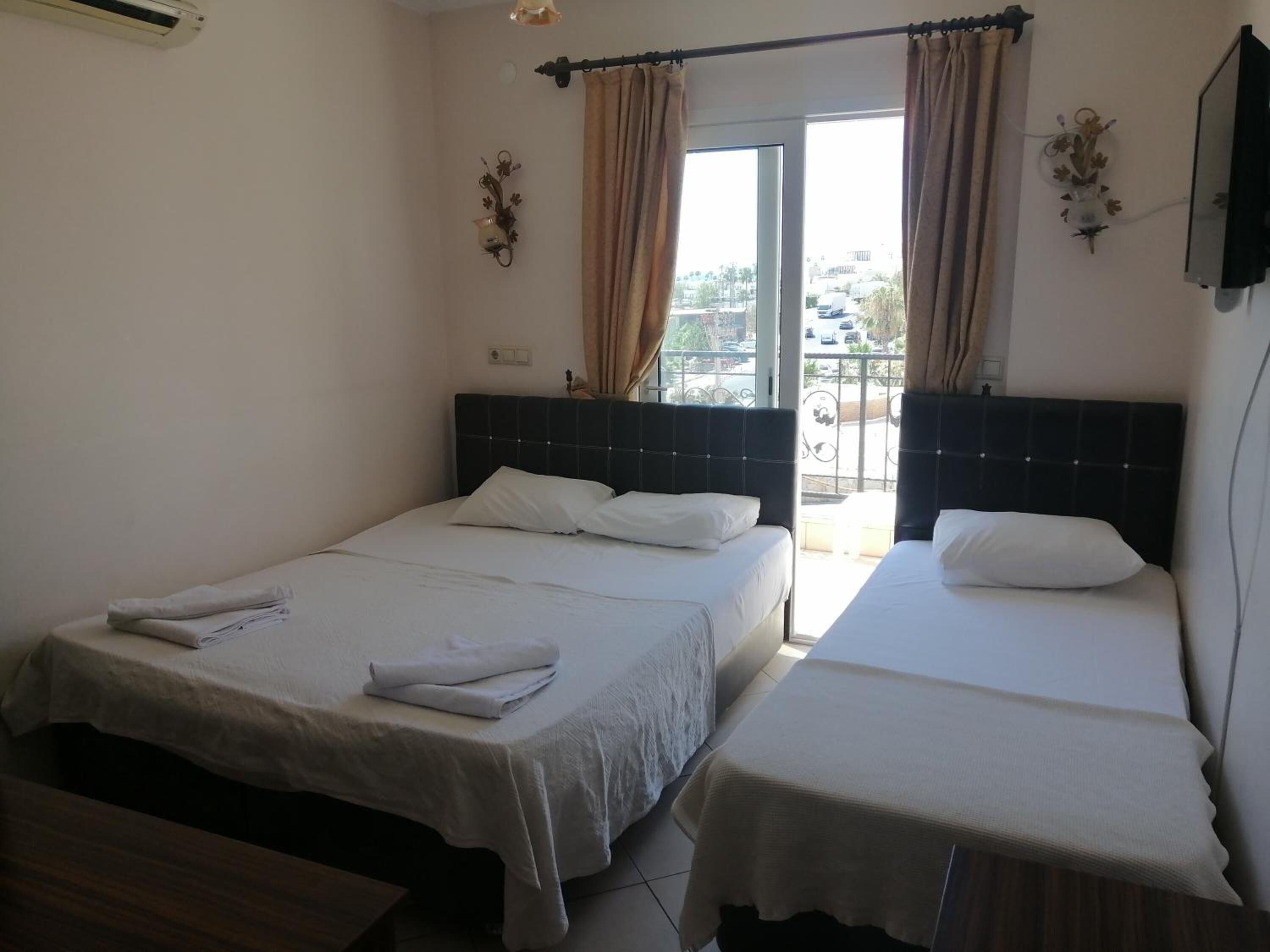 A hotel room with two beds, a window with curtains, a wall-mounted TV, and a small table.