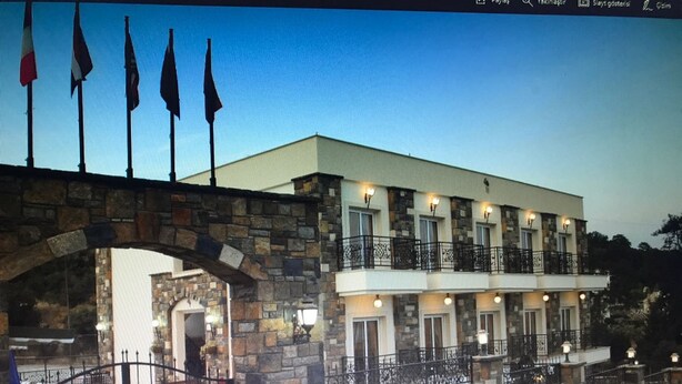 A two-story building with a stone archway entrance, multiple balconies, and a gated driveway. - Gloria Tibi Hotel Gumbet (Bodrum)