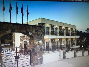 Un edificio de dos plantas con un arco de piedra en la entrada, varios balcones y un camino de acceso con portones.