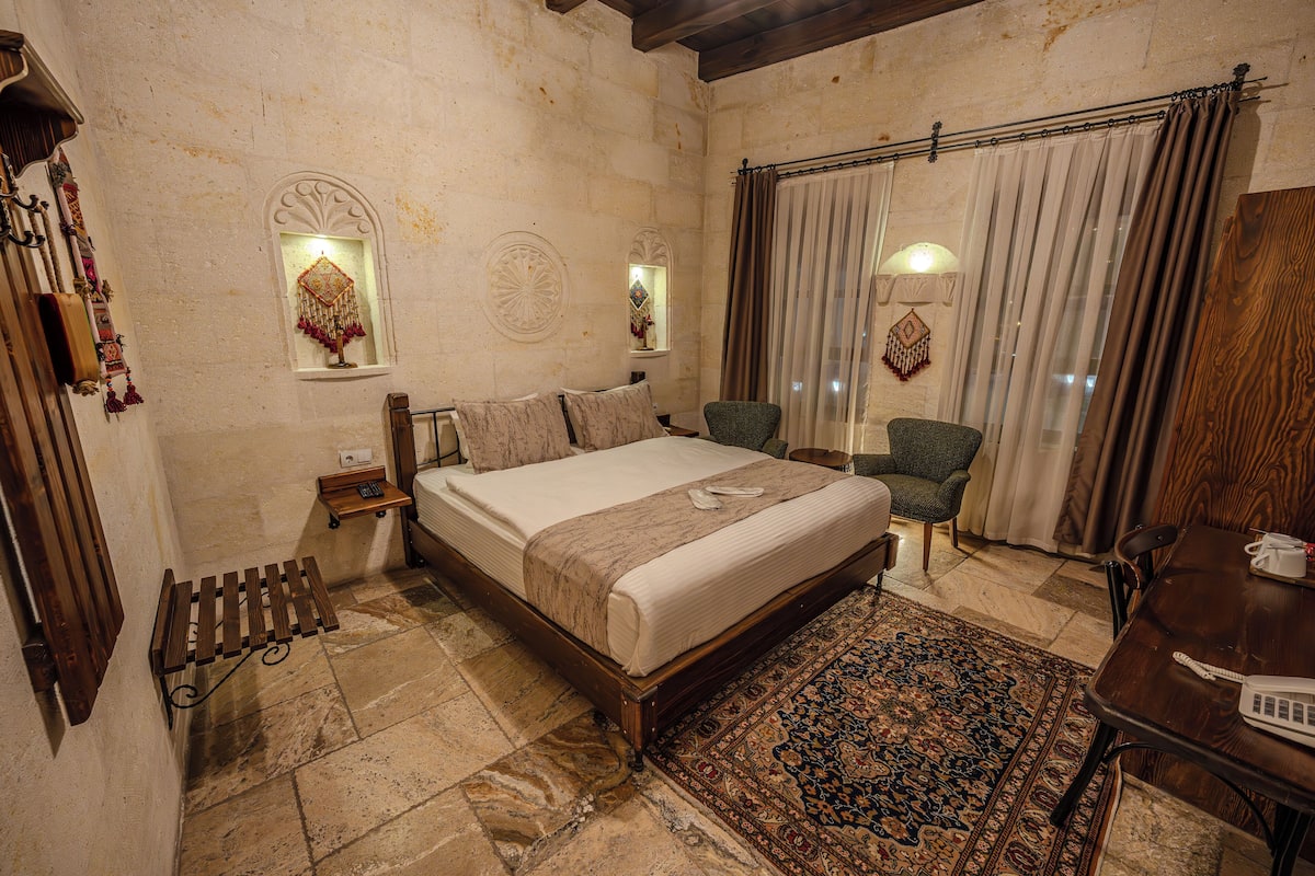 A bedroom with a large bed, a chair, a small table, and a window with curtains.