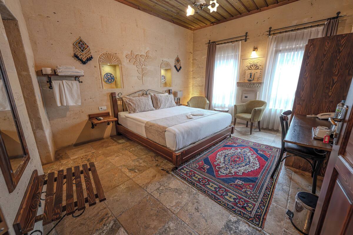 A bedroom with a bed, a desk, a chair, a rug, and a mirror.
