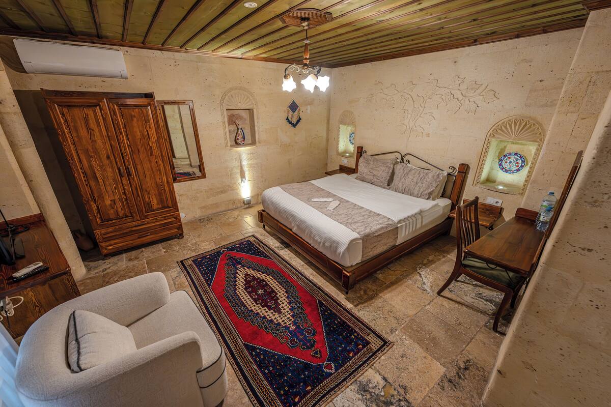 A bedroom with a bed, a wooden wardrobe, a chair, a table, and a decorative rug.