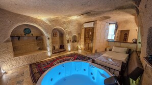 Una habitación con pared de piedra, puerta de madera, ventana, bañera y cama.