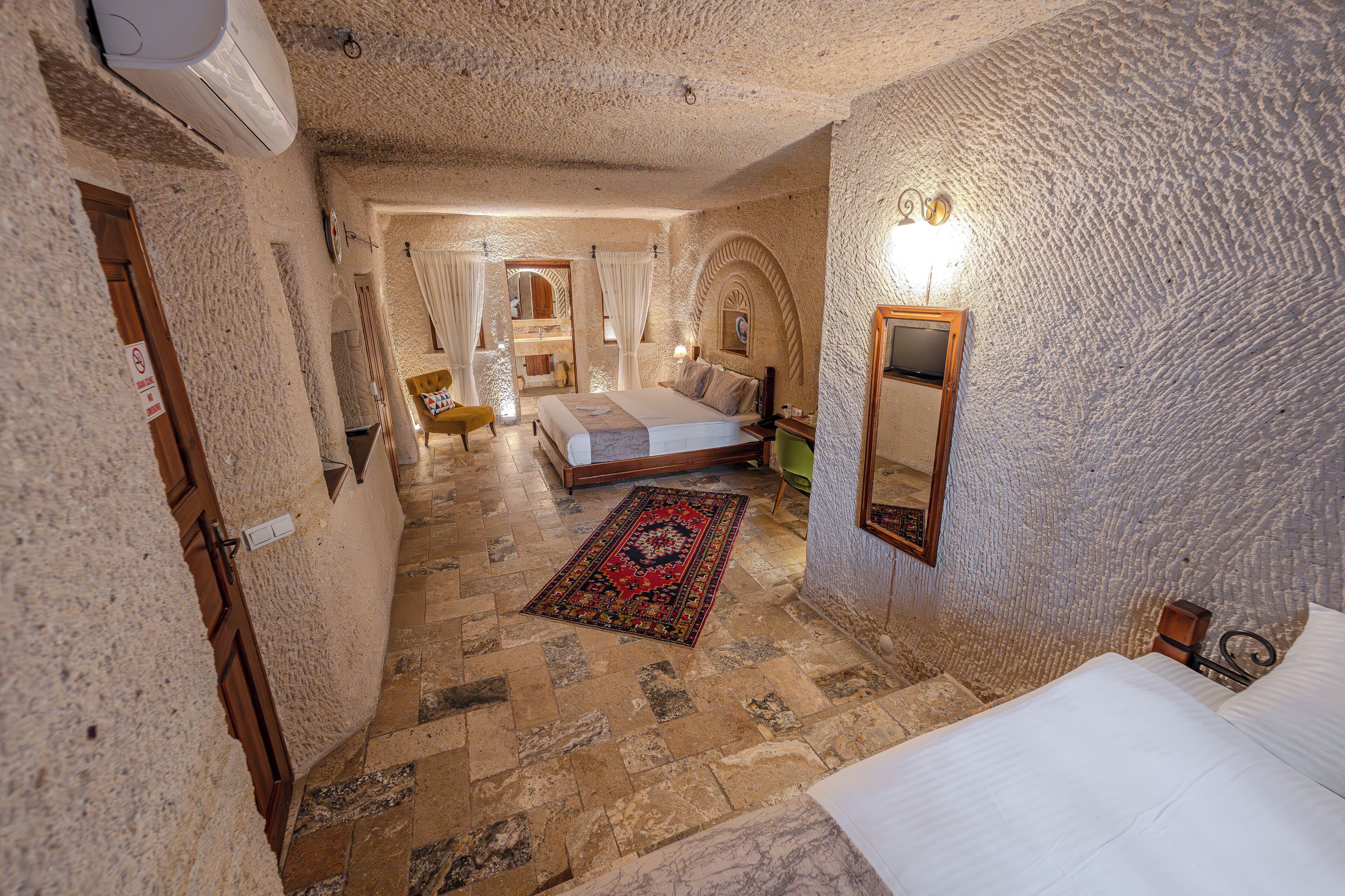 Ein Schlafzimmer mit Steinfußboden, einem Bett, einem Nachttisch, einem Spiegel und einer Tür.