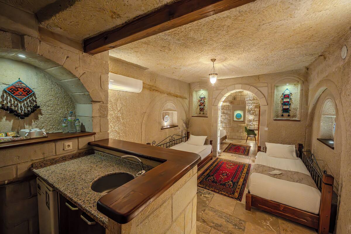 A rustic room with a stone wall, a wooden bed, a stone sink, and a small kitchen area.