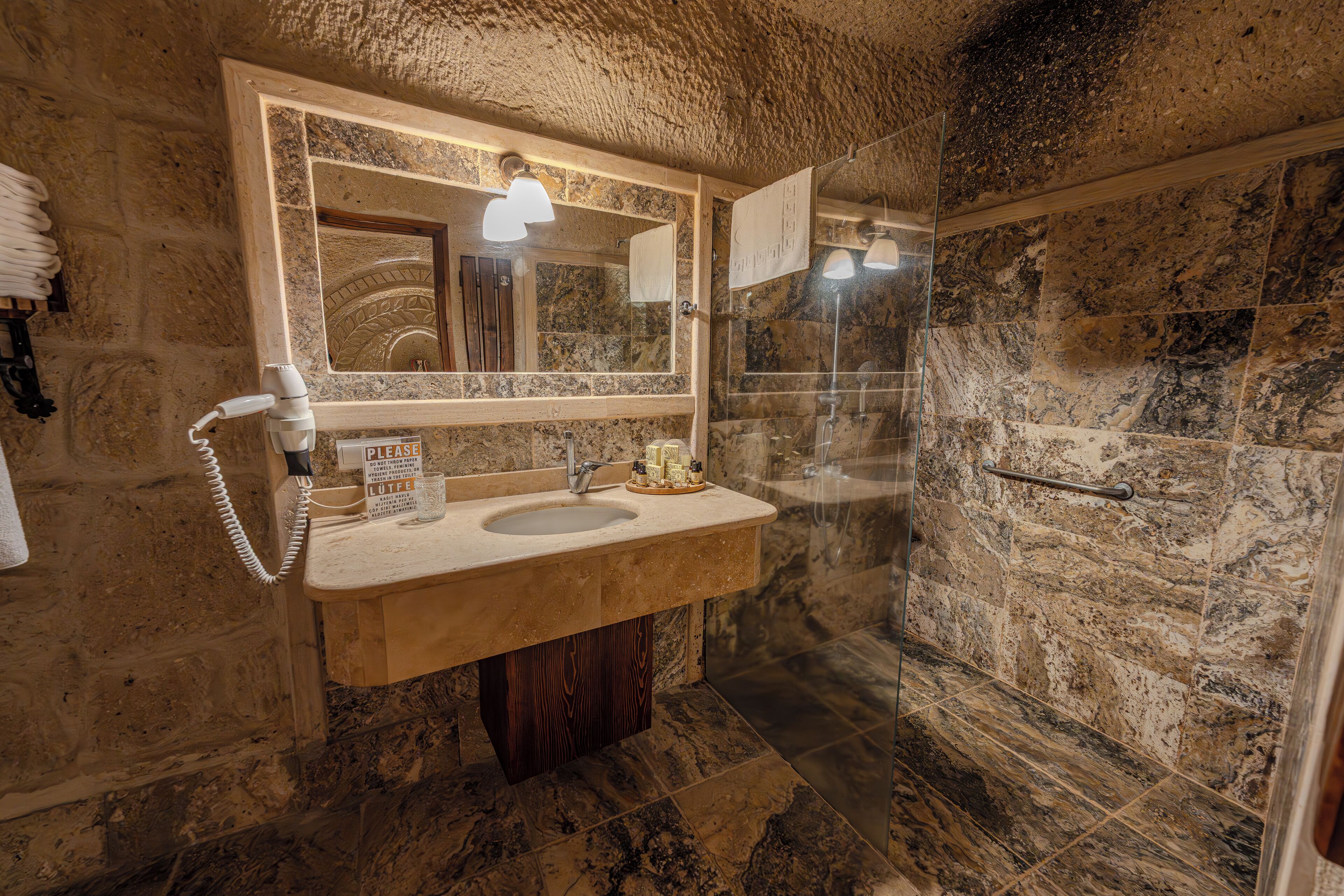 A bathroom with a stone wall, a sink with a mirror, a towel rack, and a shower area.