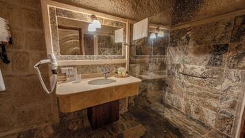 A bathroom with a stone wall, a sink with a mirror, a towel rack, and a shower area.