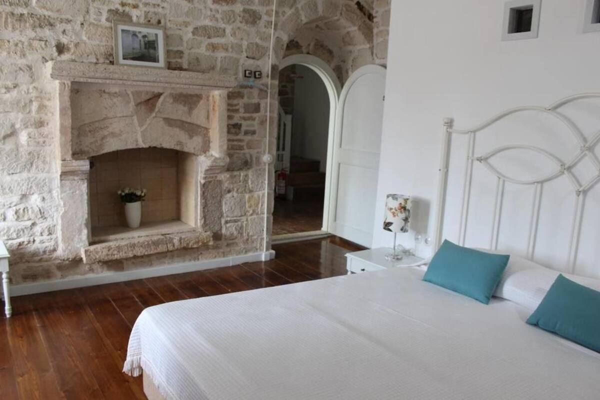 A bedroom with a stone fireplace, a bed with white bedding, and a white headboard.