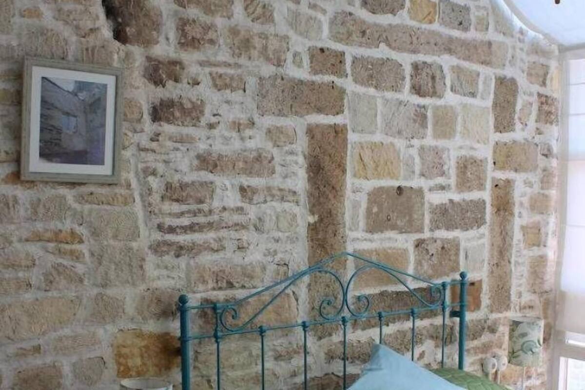A bedroom with a stone wall, a bed with green bedding, a small bedside table with a lamp, and a framed picture on the wall.
