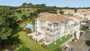 A multi-story hotel with a swimming pool, outdoor seating, and a view of the surrounding greenery. - Madame Vacances Les Palmiers du Golf (Moliets-et-Maa)