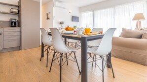A modern kitchen with a dining area, a sofa, and a TV. - Madame Vacances Les Palmiers du Golf (Moliets-et-Maa)