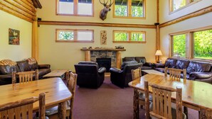 A lodge interior with a fireplace, leather seating, wooden tables, and a deer head mounted on the wall. - Adirondack Spruce Lodge (Wilmington)