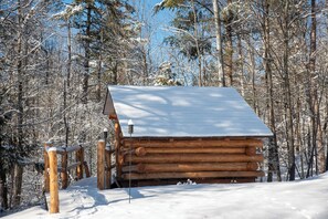 A log cabin with a snow-covered roof, surrounded by a forest. - Adirondack Spruce Lodge (Wilmington)