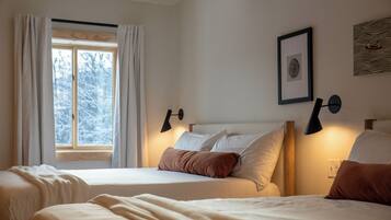 A bedroom with two beds, a window with curtains, wall-mounted lamps, and a framed picture.