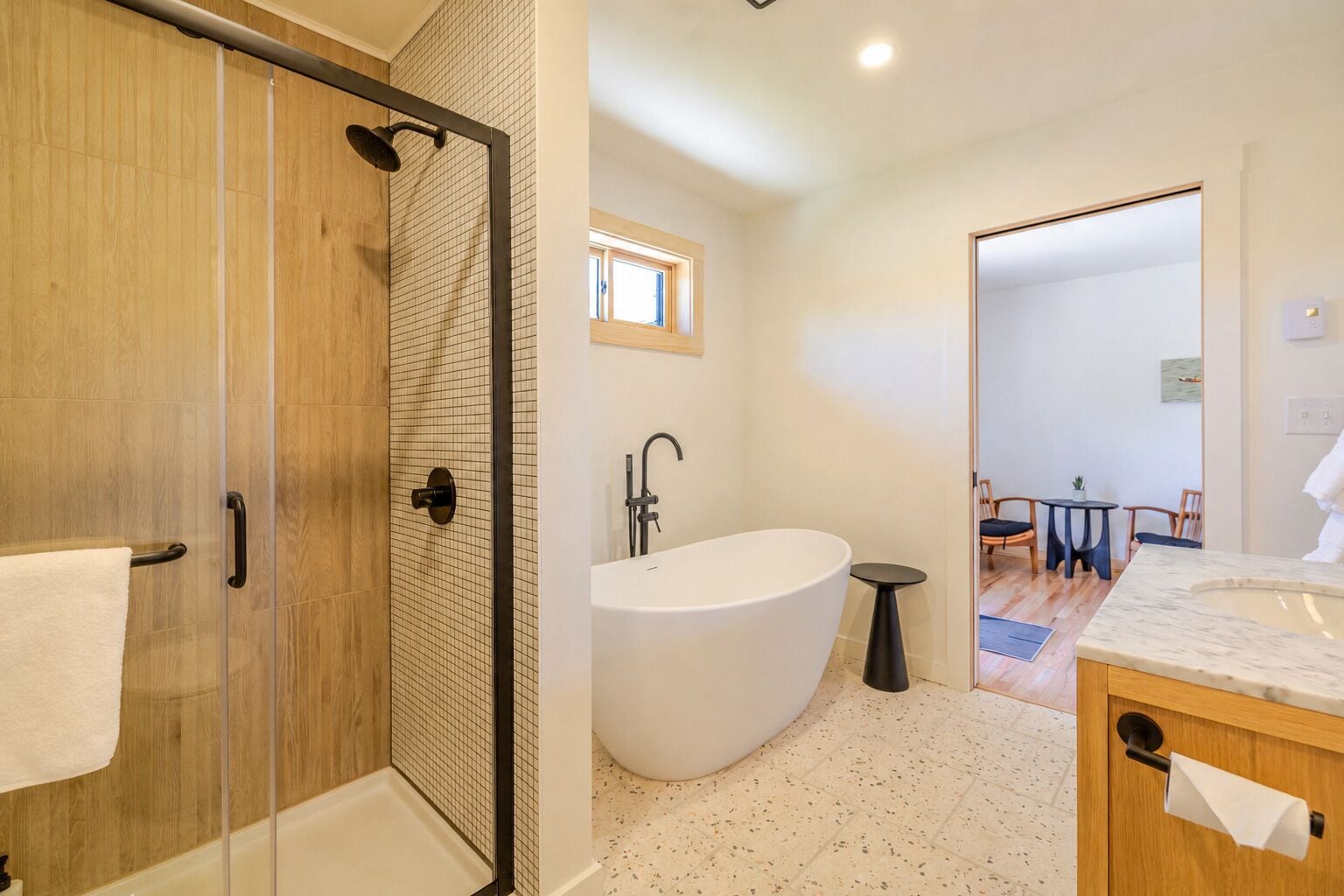 A modern bathroom with a glass-enclosed shower, a freestanding bathtub, and a wooden vanity.