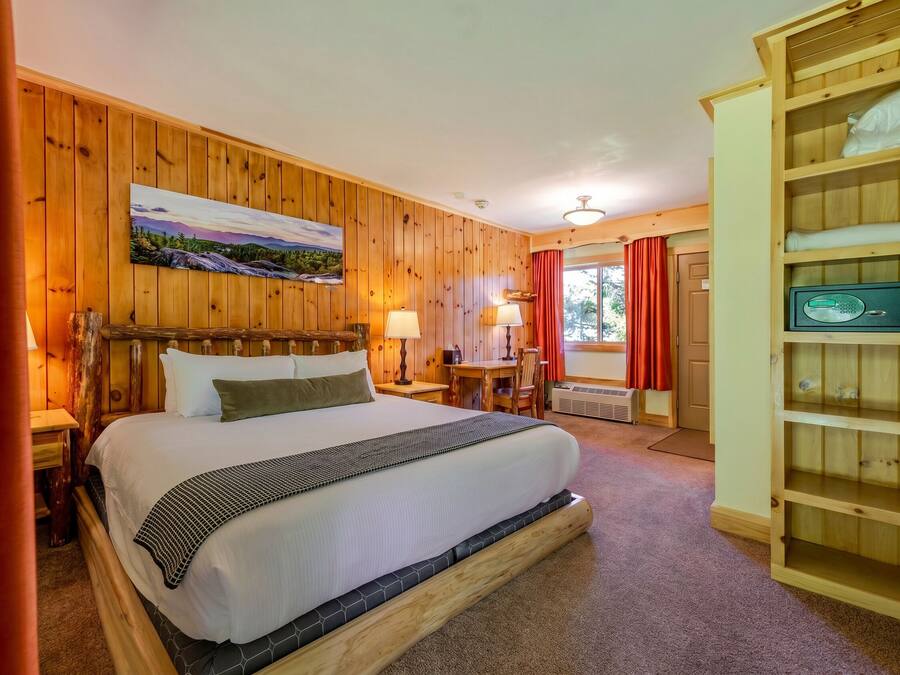 A wooden-paneled room with a large bed, a desk, and a shelving unit.