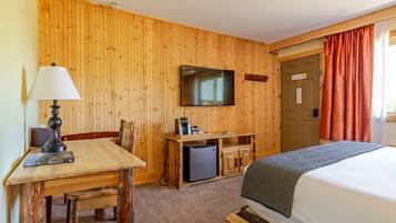 Una habitación con pared de madera, un televisor sobre un escritorio de madera, una cama con una colcha, y una puerta con un letrero.