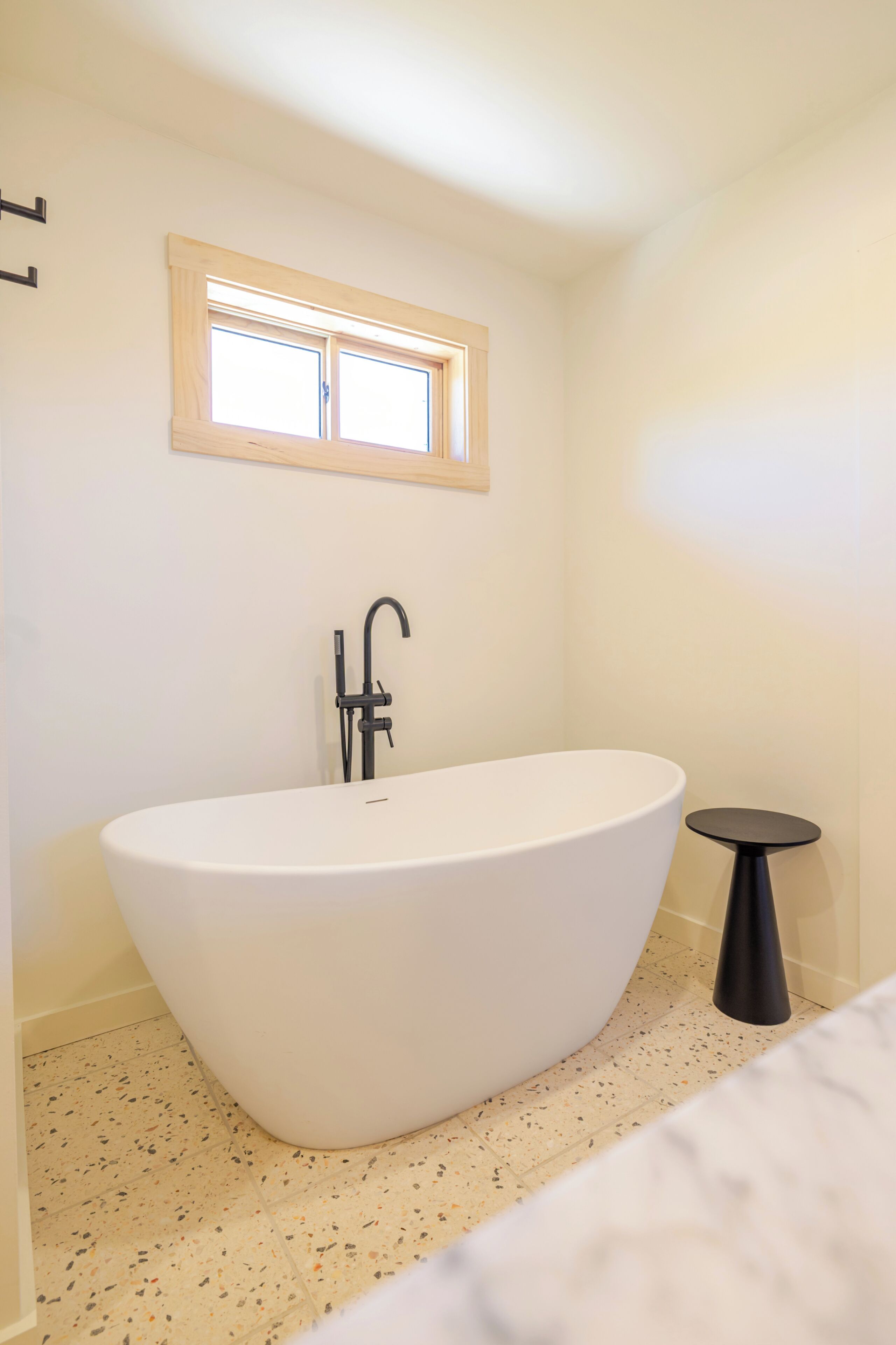 A modern bathroom with a freestanding bathtub, a small round table, and a window above the tub.