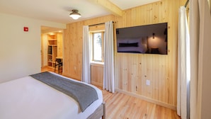 A bedroom with a bed, wooden walls, a TV, and a window. - Adirondack Spruce Lodge (Wilmington)