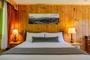 A wooden-paneled room with a bed, two bedside lamps, and a painting on the wall. - Adirondack Spruce Lodge (Wilmington)