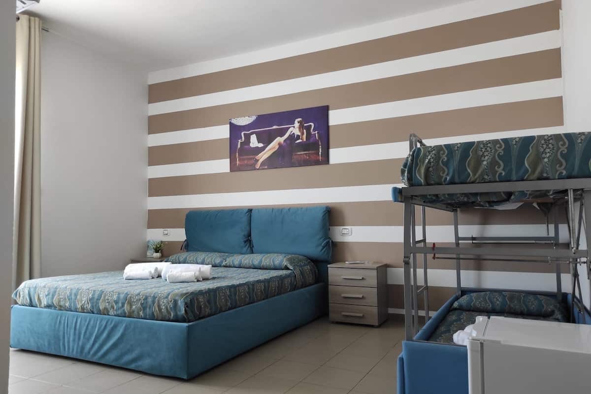 A bedroom with a striped wall, a bed with blue bedding, a bunk bed, and a small bedside table.