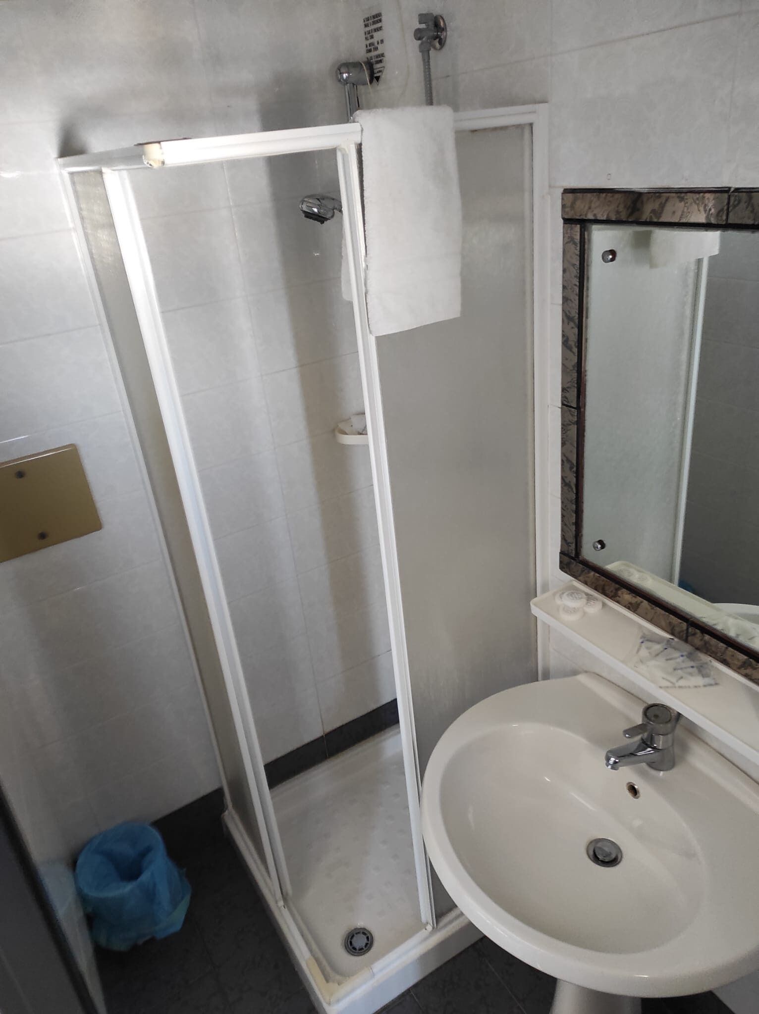 Un baño con cabina de ducha de vidrio, lavabo blanco y espejo con marco de mármol.