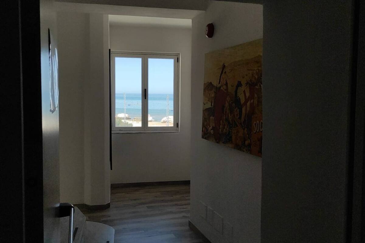 A hallway with a large window offering a view of the sea and a painting on the wall.