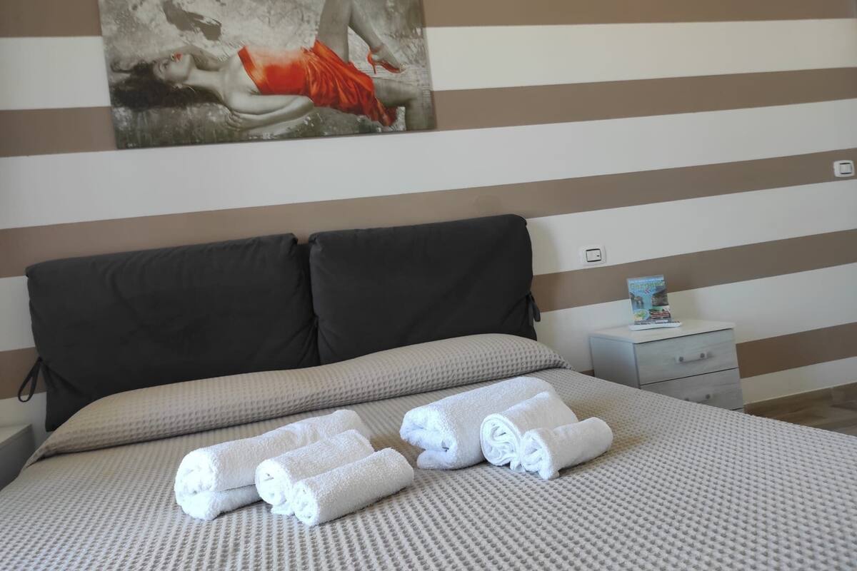 A neatly made bed with rolled white towels, a dark headboard, and a striped wall with a painting above.