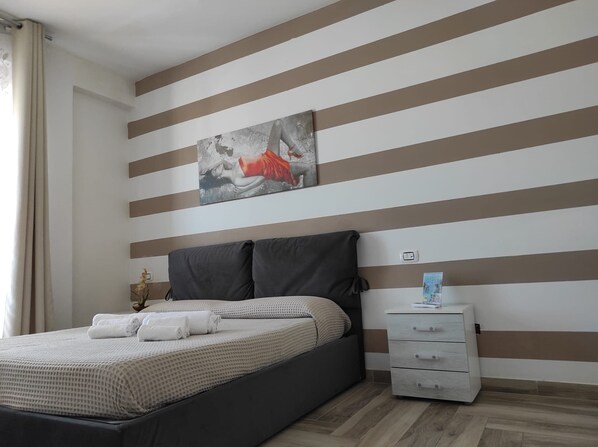 A modern bedroom with a bed, a nightstand, and a painting on the wall. - My Hotel (Rodi Garganico)