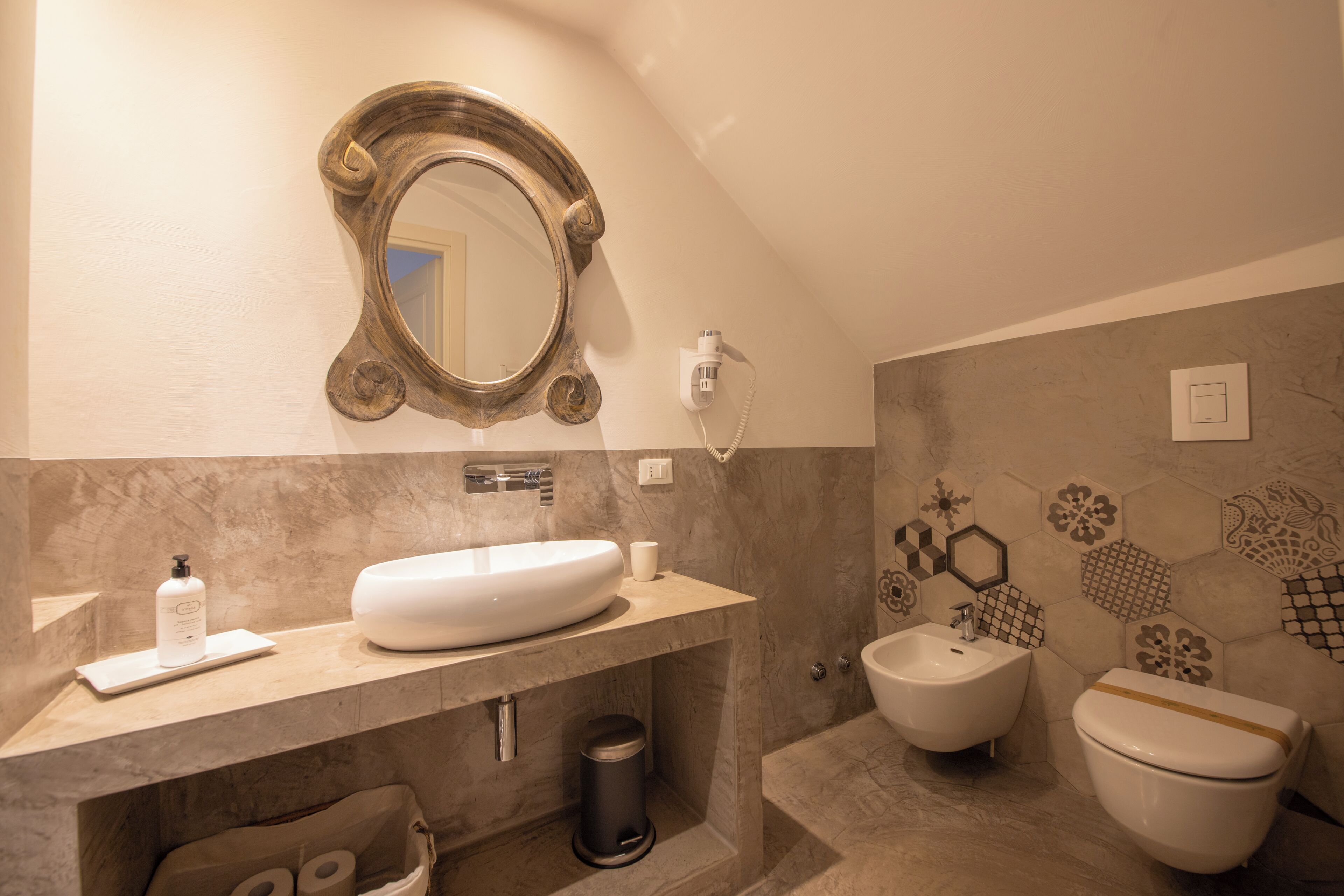A bathroom with a sink, bidet, toilet, mirror, and a trash can.