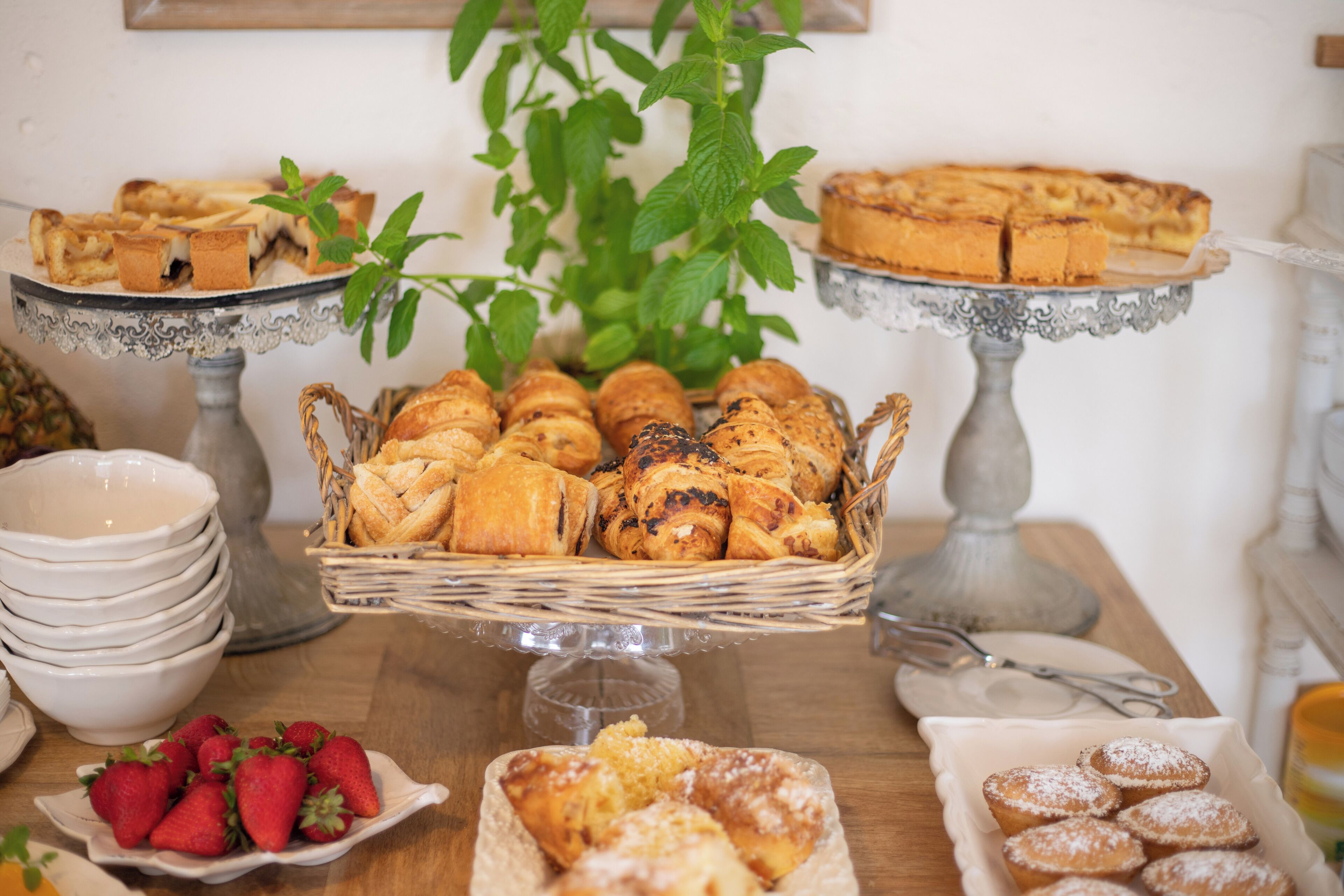 Une table de buffet proposant une variété de produits de boulangerie, notamment des pâtisseries et du pain, présentés sur des présentoirs et dans des paniers.