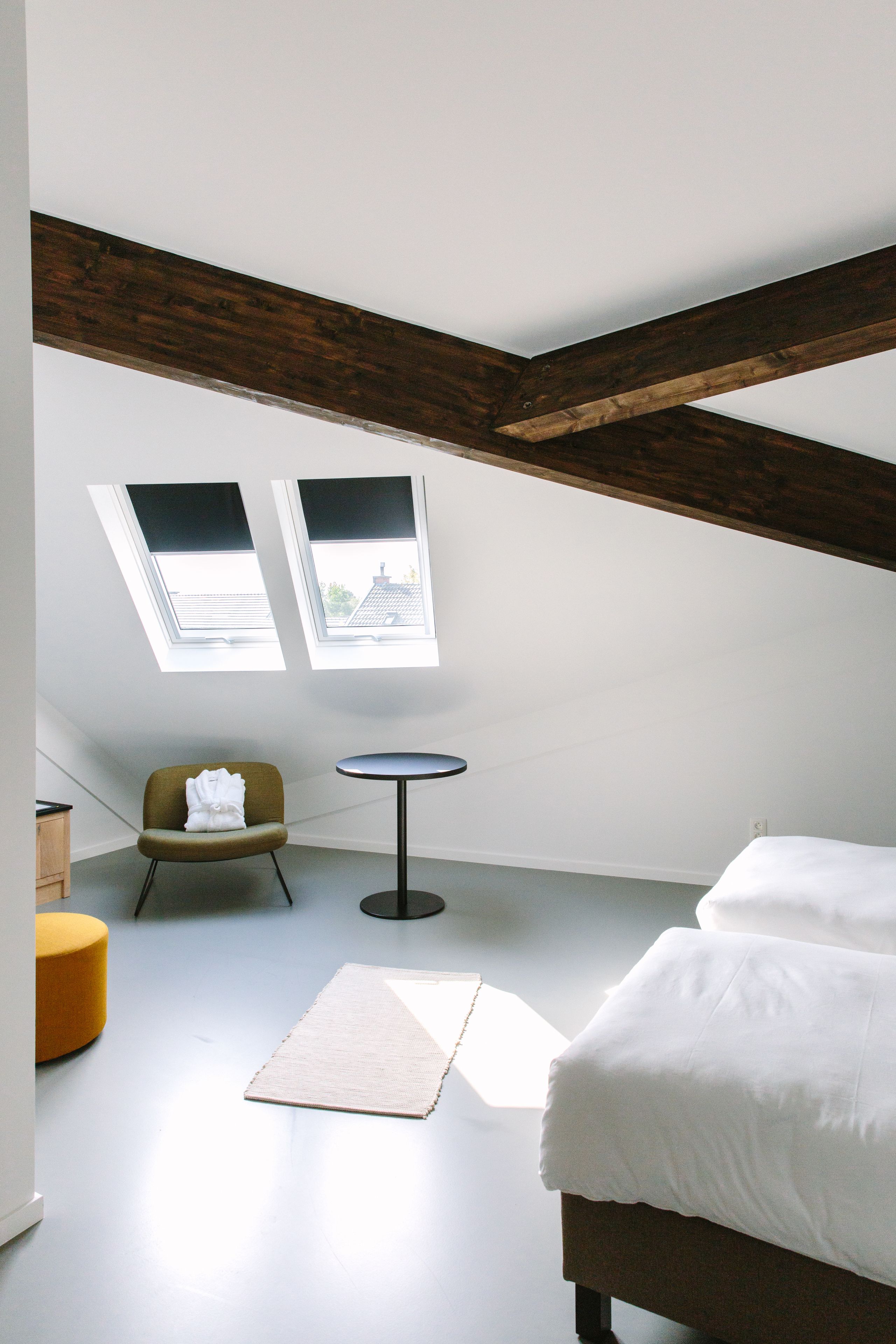 Una habitación con cama, una mesita, una silla y dos tragaluces.
