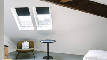 Una habitación con cama, una mesita, una silla y dos tragaluces.
