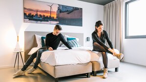 Habitación de hotel moderna con una cama grande, una mesita de noche con lámpara y un ventanal con cortinas.