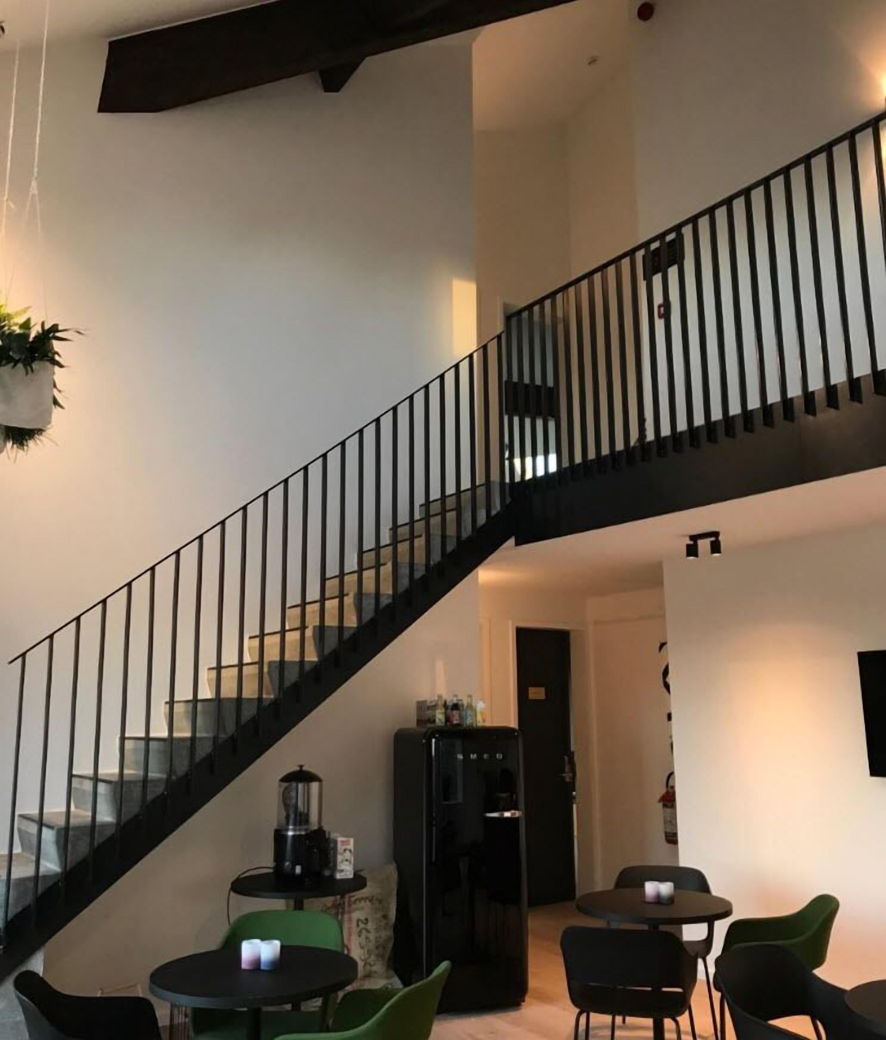 A modern interior with a black staircase, a kitchen area, and a dining space with green chairs.
