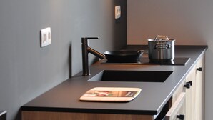 Una cocina moderna con encimera oscura, un fregadero, una estufa y una olla sobre la hornilla.
