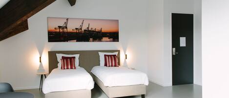 A hotel room with two beds, a large window, a painting of a sunset, and a door.
