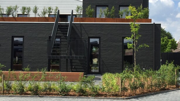 Un edificio moderno con fachada negra, una terraza de madera y una escalera que lleva a un nivel superior.