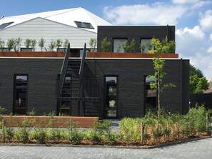 A modern building with a black facade, a wooden deck, and a staircase leading to an upper level. - TRUST Hotel (Beveren)