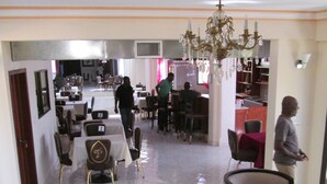 A spacious dining area with multiple tables and chairs, a chandelier, and a kitchen in the background. - Tabarre's Palace (Tabarre)